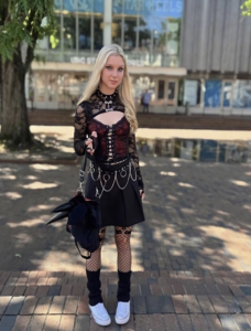 A female college student with long blonde hair wearing a black and red outfit with silver chains poses for a photo in the Pit at UNC-Chapel Hill