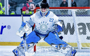 Joel Hughes, wearing a black beanie on top of his goalie helmet and light blue and white pads, stands in goal at the Frozen Finley game at Carter-Finley Stadium on Feb. 20, 2023.
