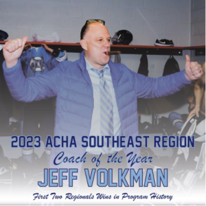 UNC club hockey head coach Jeff Volkman, wearing a blue jacket, light blue shirt, and white and light blue tie gives two thumbs-ups as he smokes a cigar in the team locker room. This graphic congratulates Volkman on being named 2023 ACHA Southeast Region Coach of the Year.