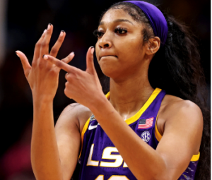 Wearing a purple and gold jersey and purple headband, LSU forward Angel Reese taps her right ring finger.